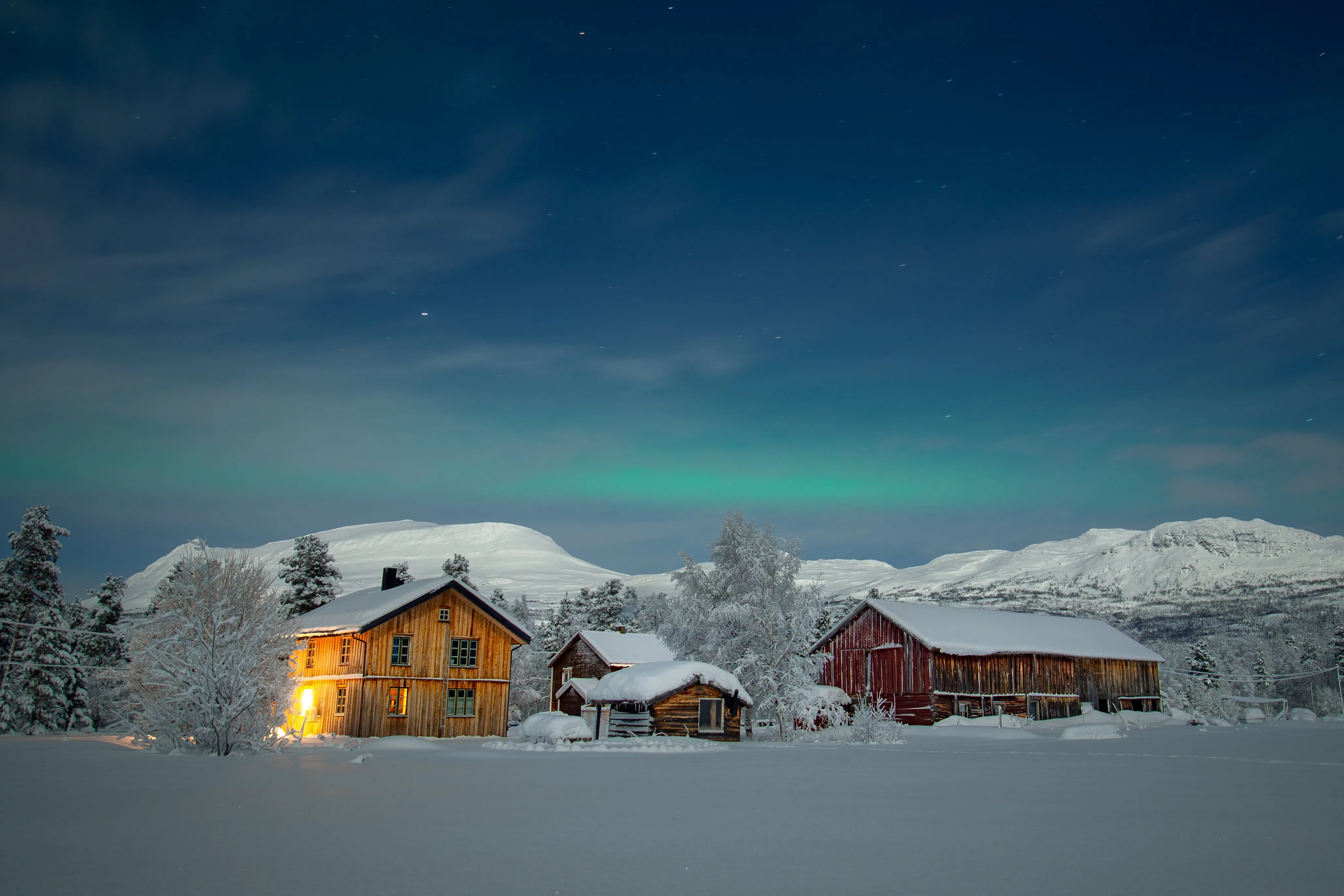 Warmly lit cabin standing in a vast, snow-covered landscape under a dark sky.
