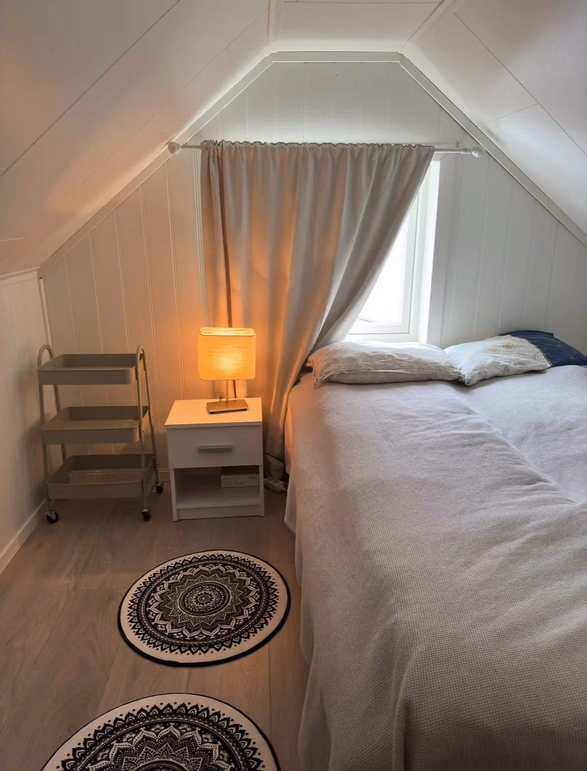 Cozy attic bedroom with a bed and warm lamp beneath a sloping ceiling.