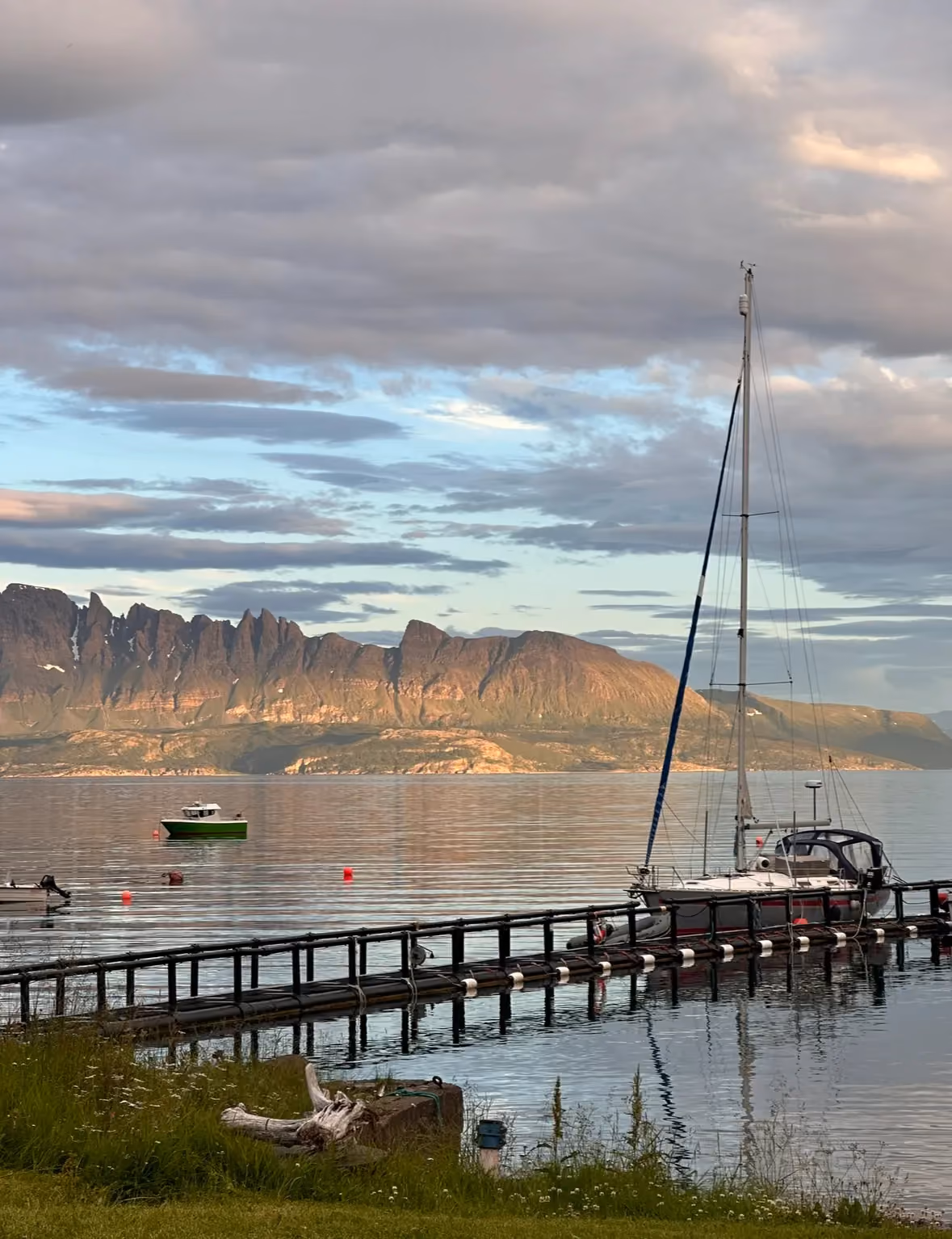 Wooden dock stretching into a calm fjord under a moody twilight sky.