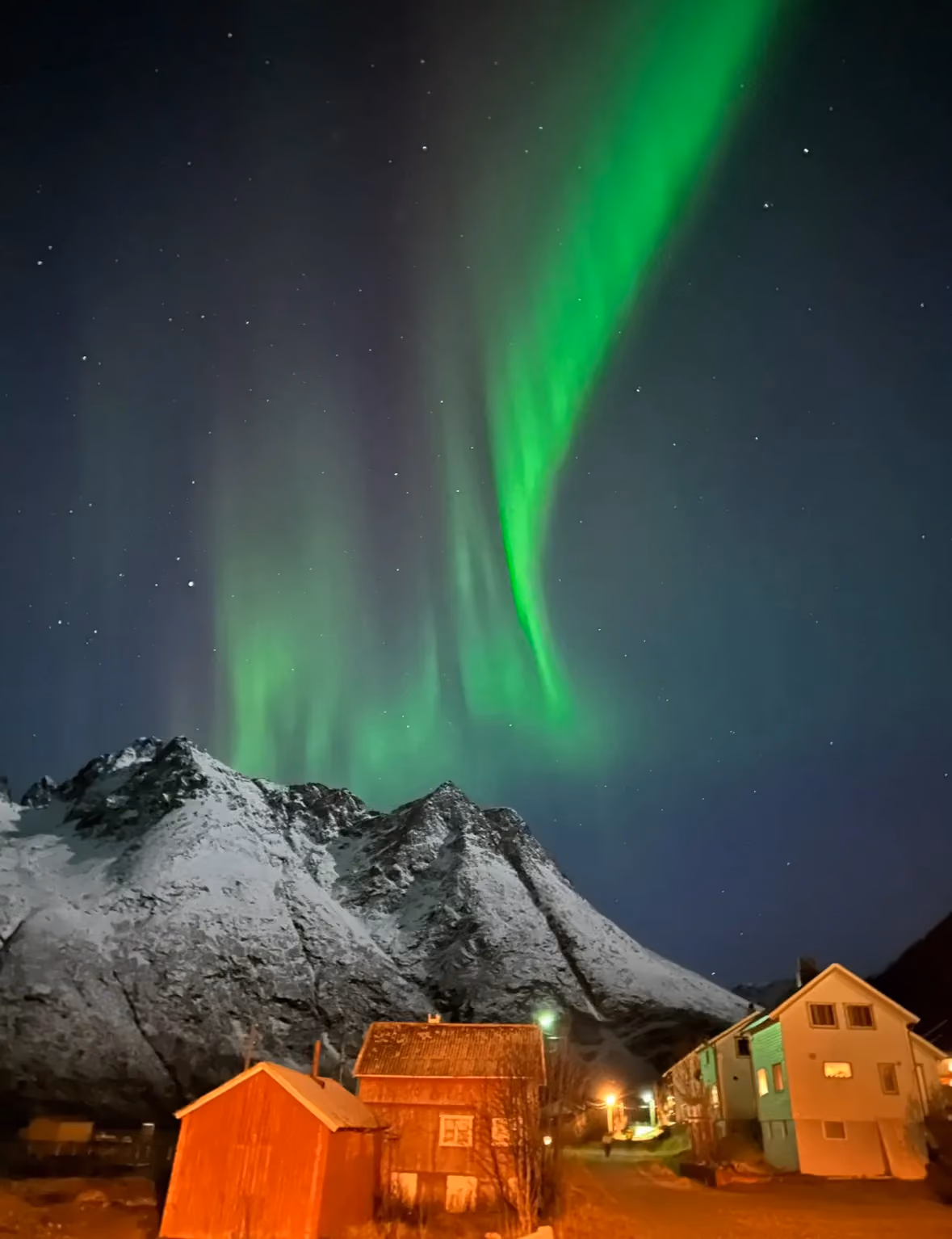 Green northern lights beaming into the night sky behind small lit Halloween decorations.