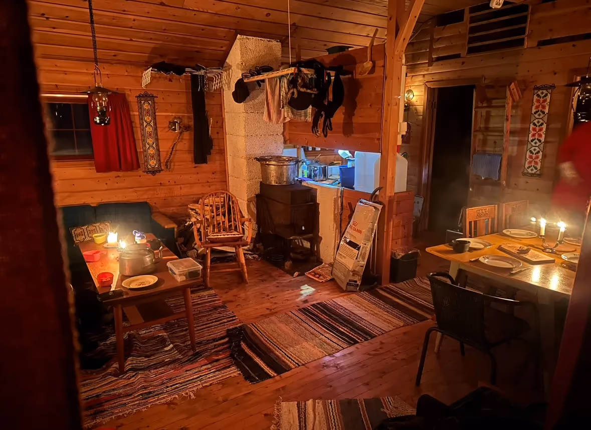 Warmly lit wooden cabin living room with cozy armchairs and a wood stove.
