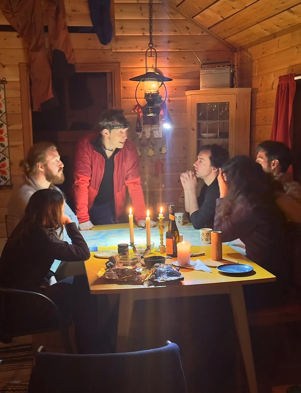 Friends gathered around a dining table inside a rustic log cabin at night.