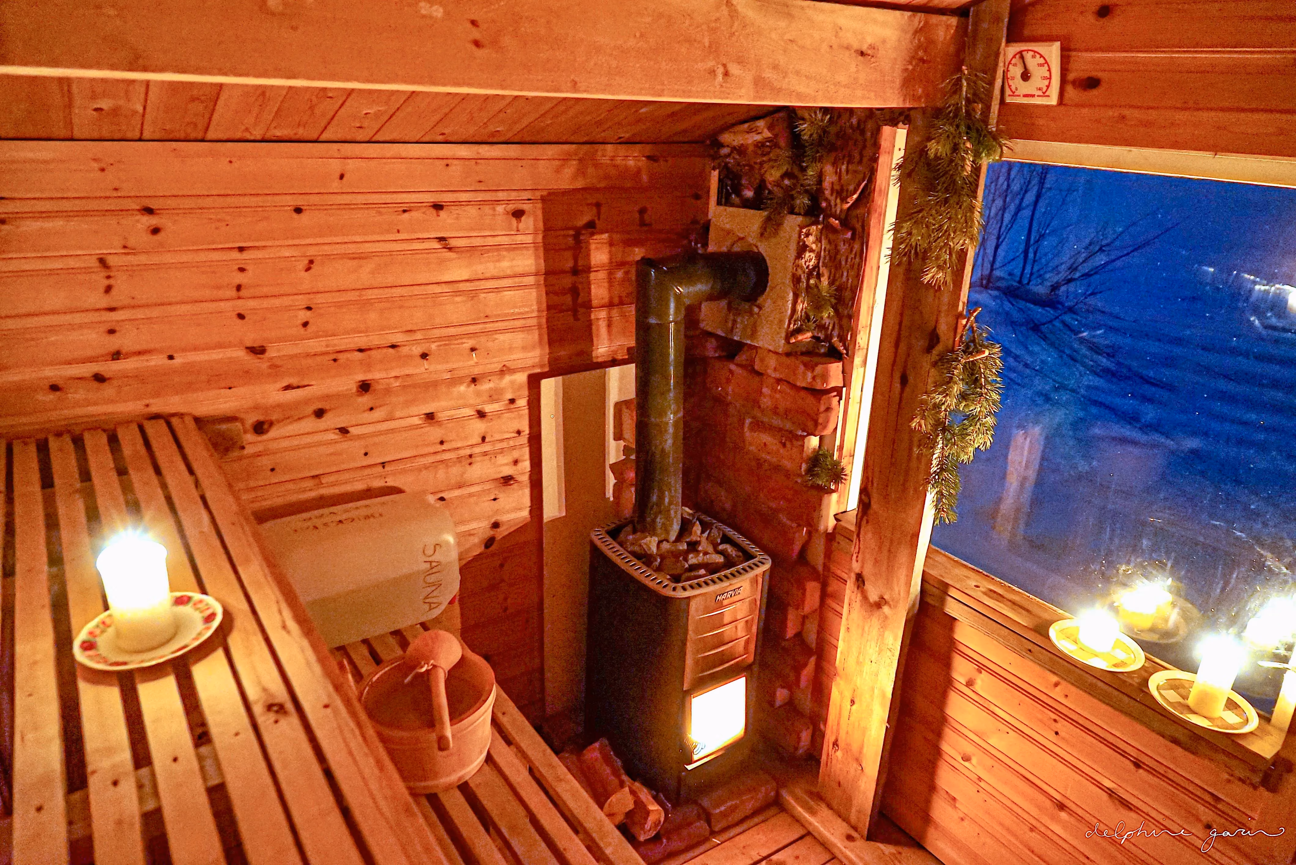 Interior of a cozy wooden sauna warmly illuminated by candles and a stove.