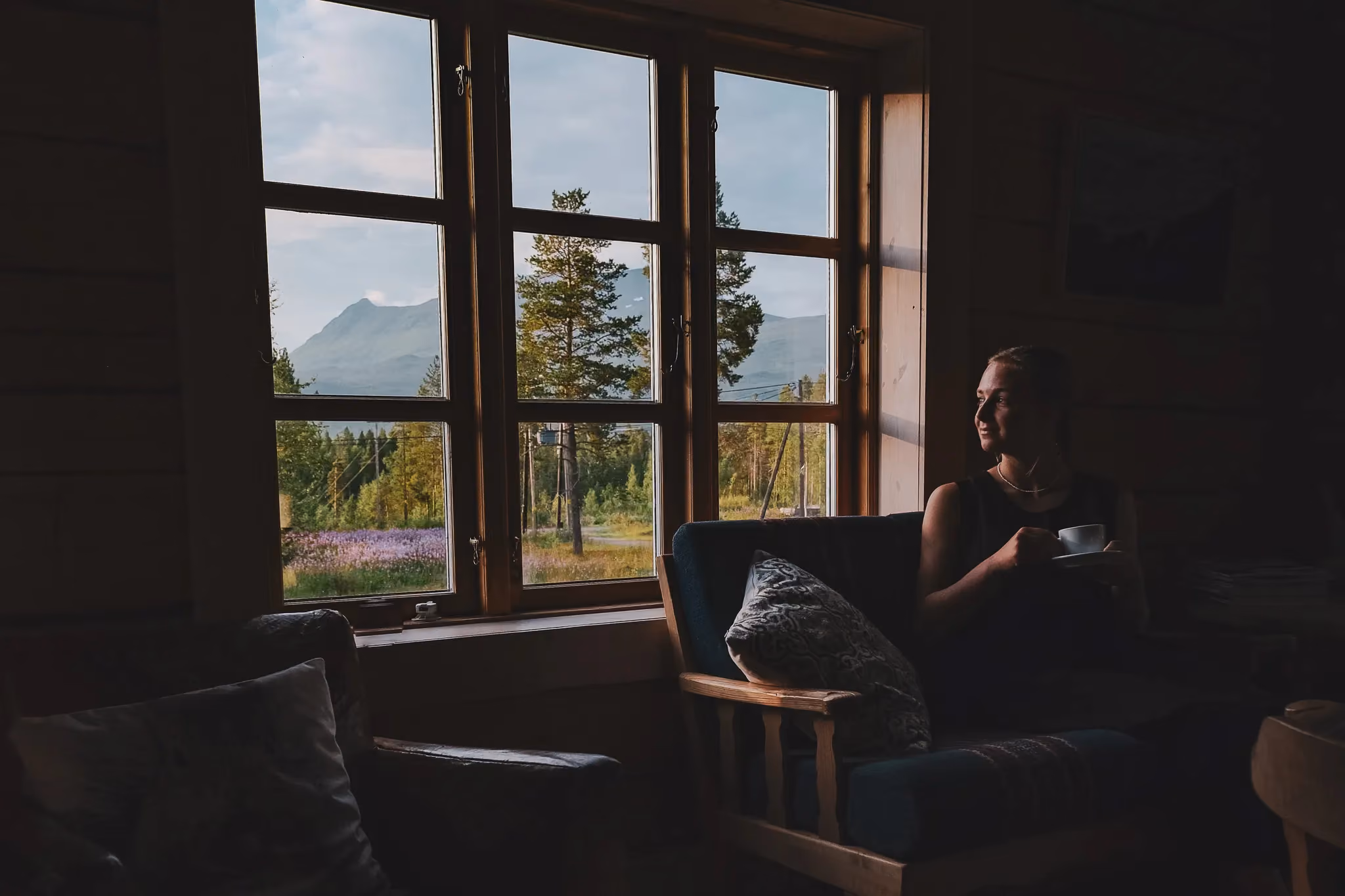 Cozy, dimly lit living room with large windows overlooking trees outside.