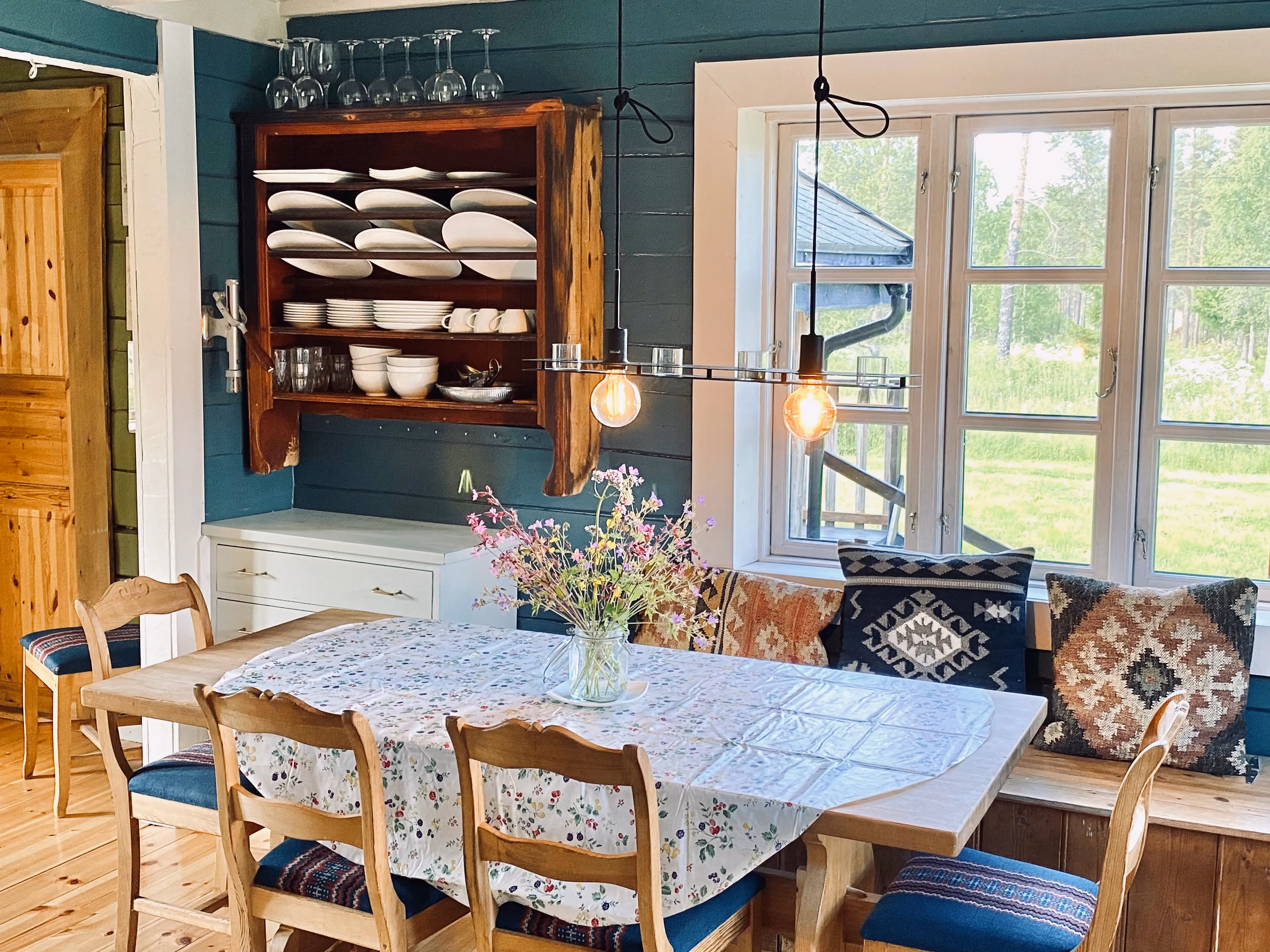 Bright dining area with a long white table, wooden chairs, and a teal accent wall.
