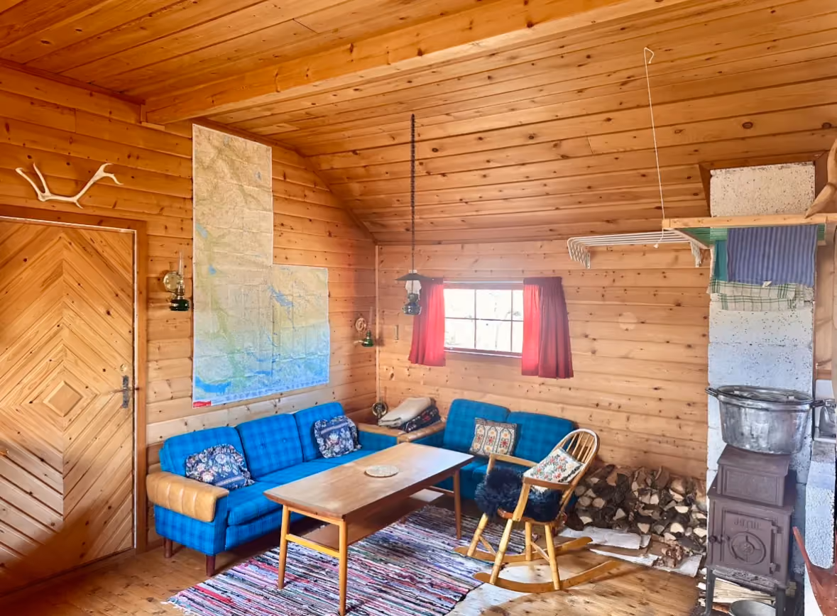 Interior of a wooden cabin featuring a blue sofa, table, and warm lighting.