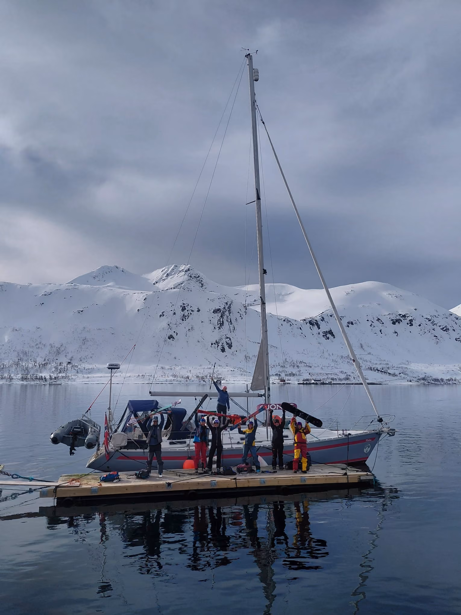 Sailboat with passengers on deck anchored before a snow-capped mountain backdrop.