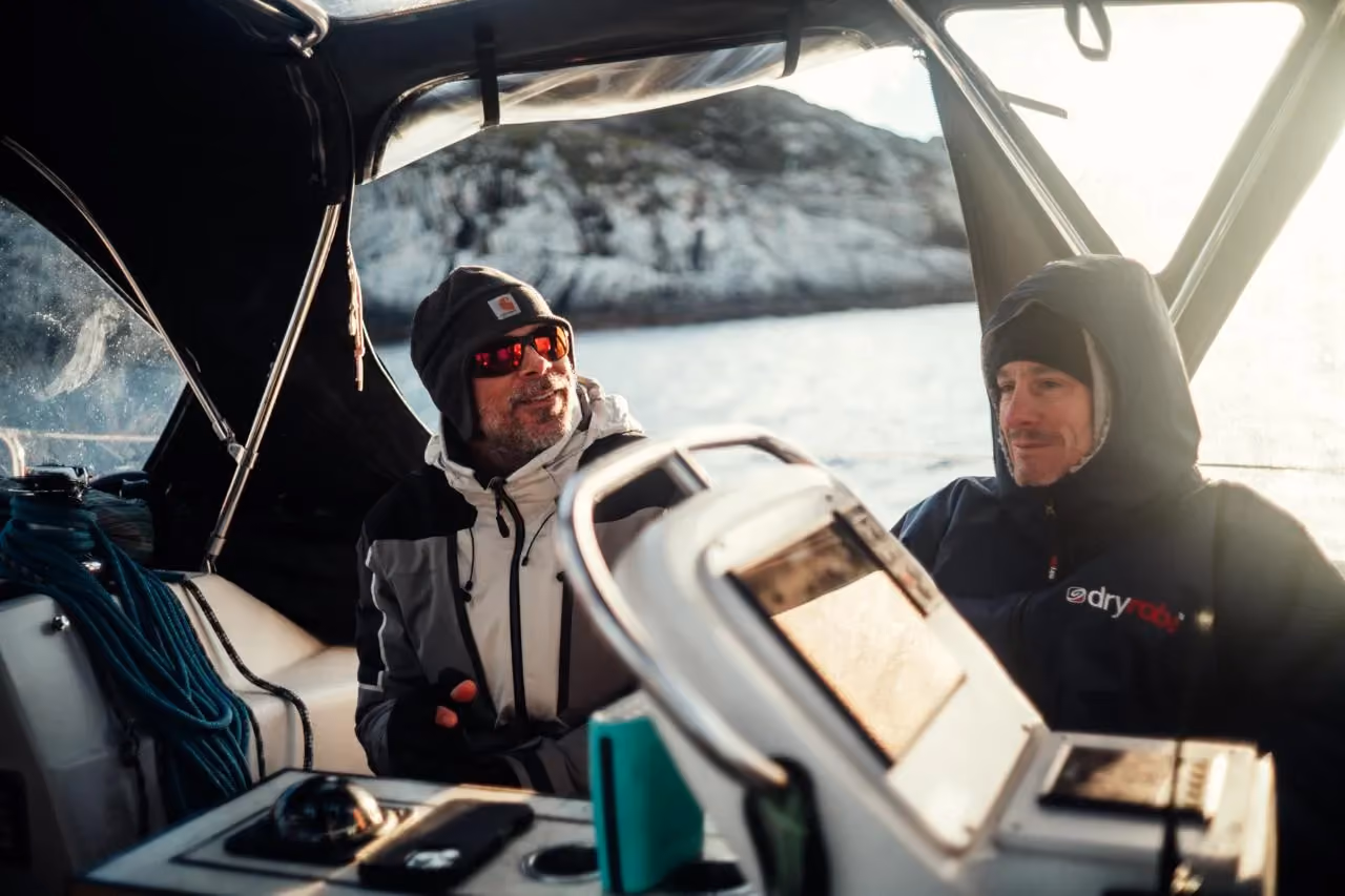 Two people at the helm and navigation controls inside a boat cockpit.