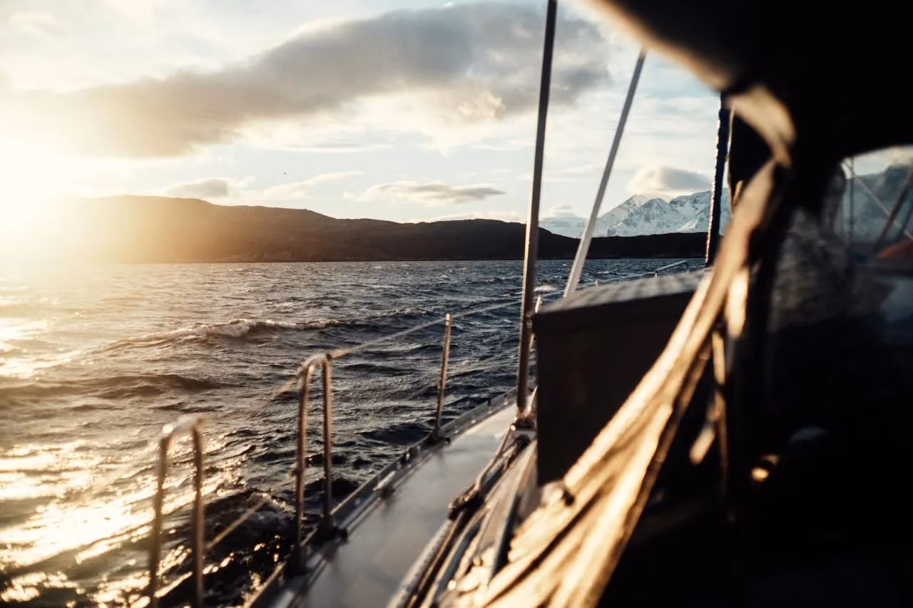 View from a sailboat deck looking toward a bright golden sunset over open sea.