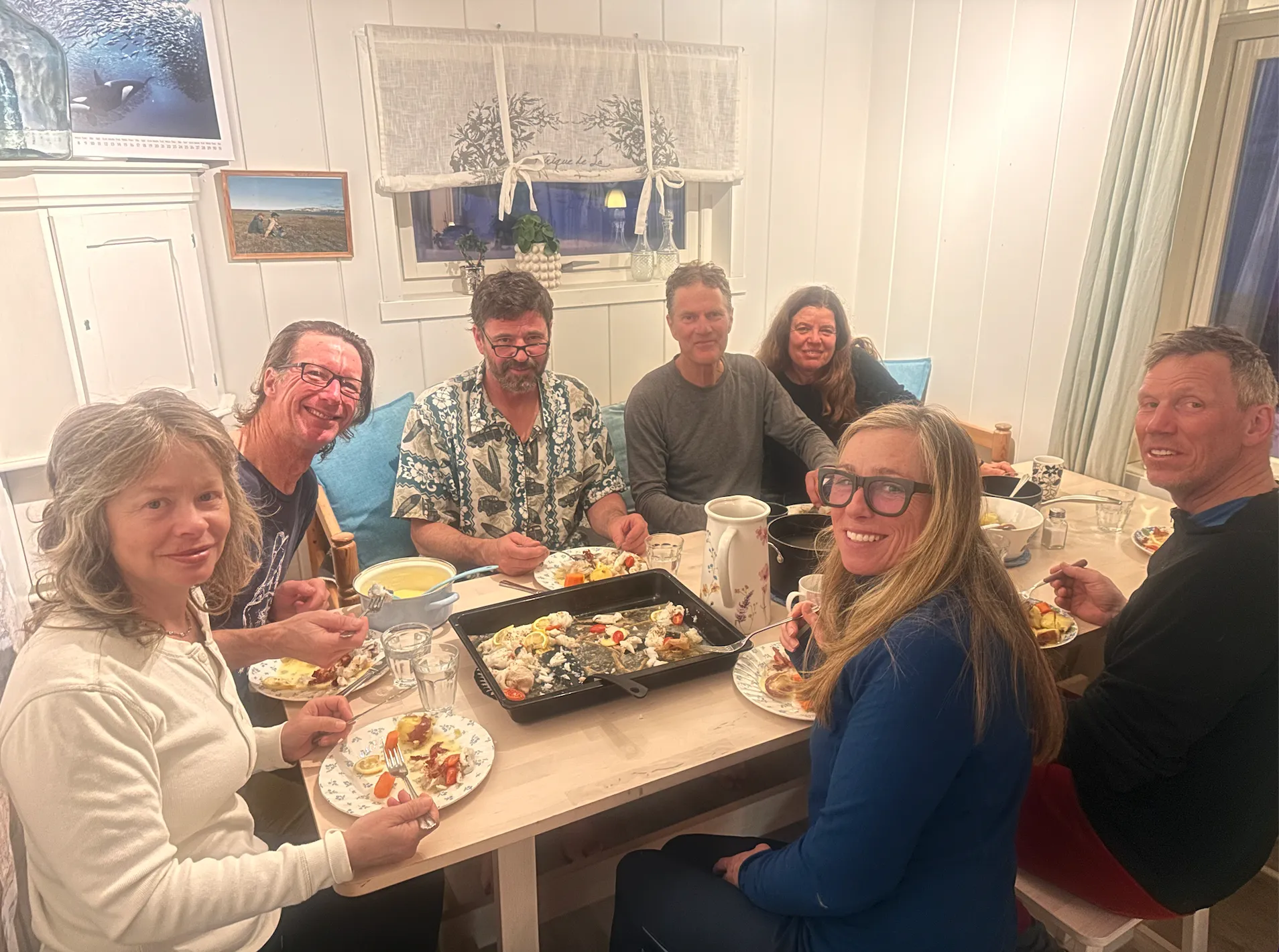 Group of people enjoying a meal together around a long wooden dining table indoors.