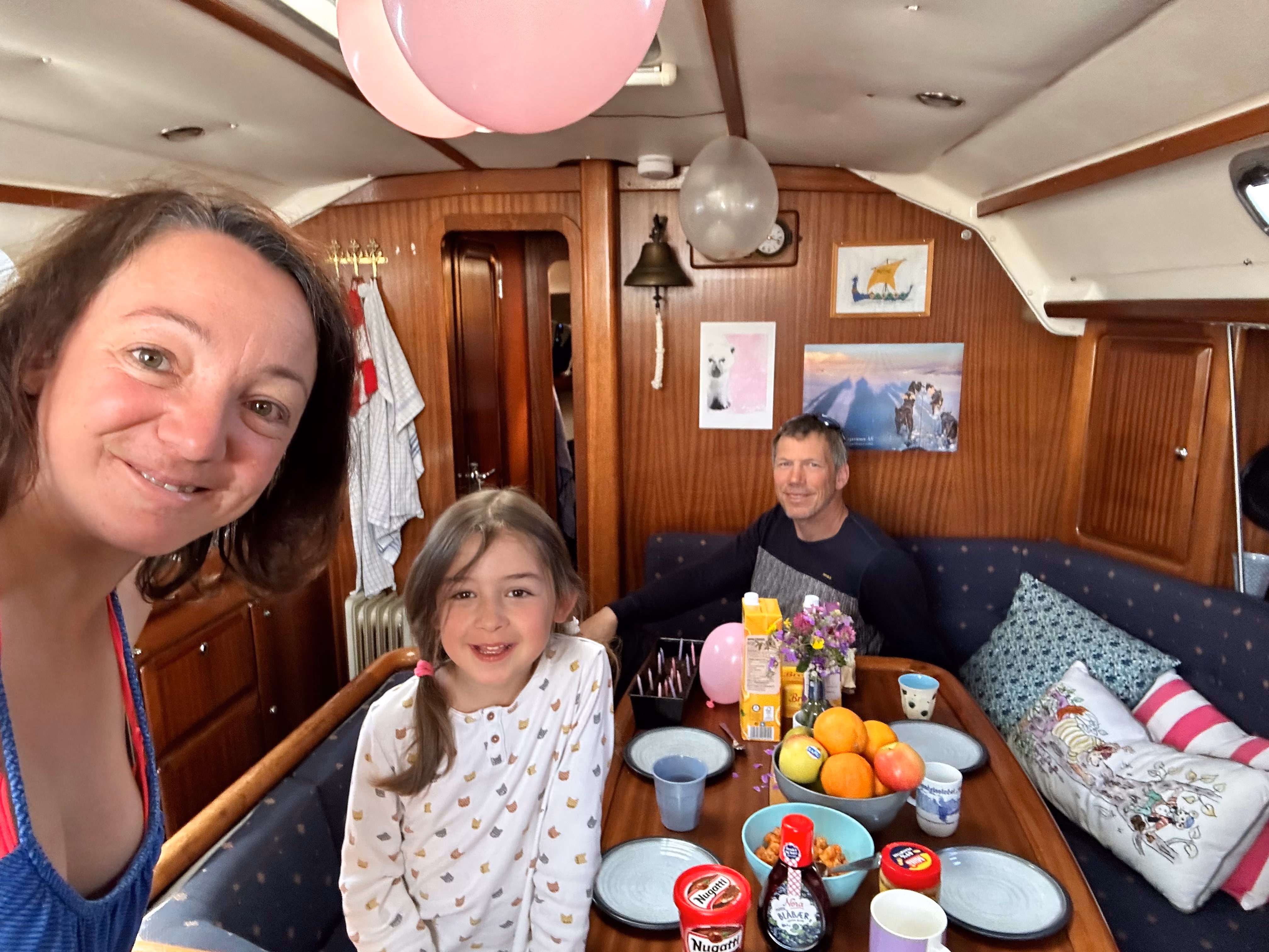 Family taking a group selfie around a table with food inside a boat cabin.