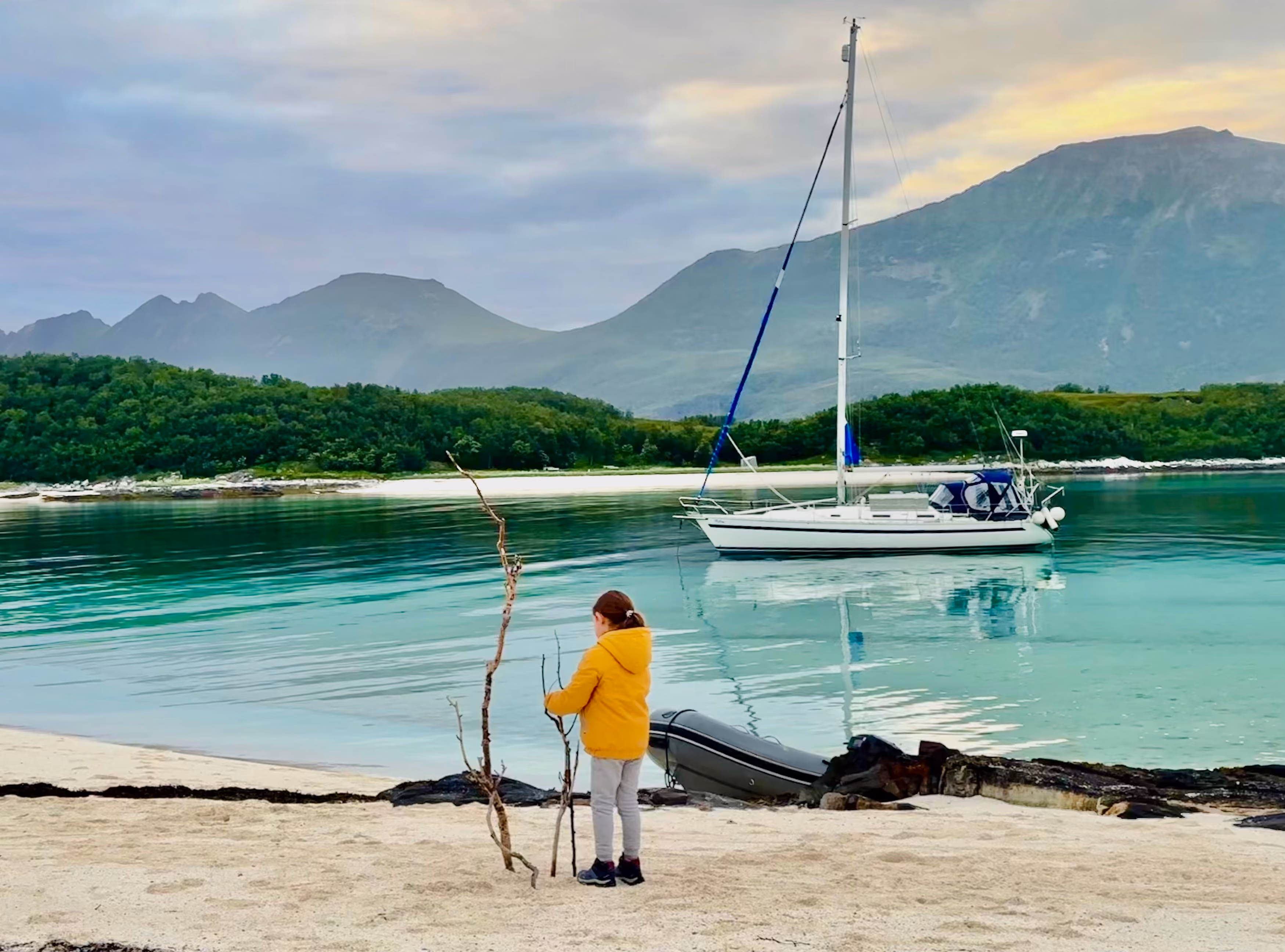 Sailboat anchored in a calm turquoise bay next to a sandy beach and green mountains.