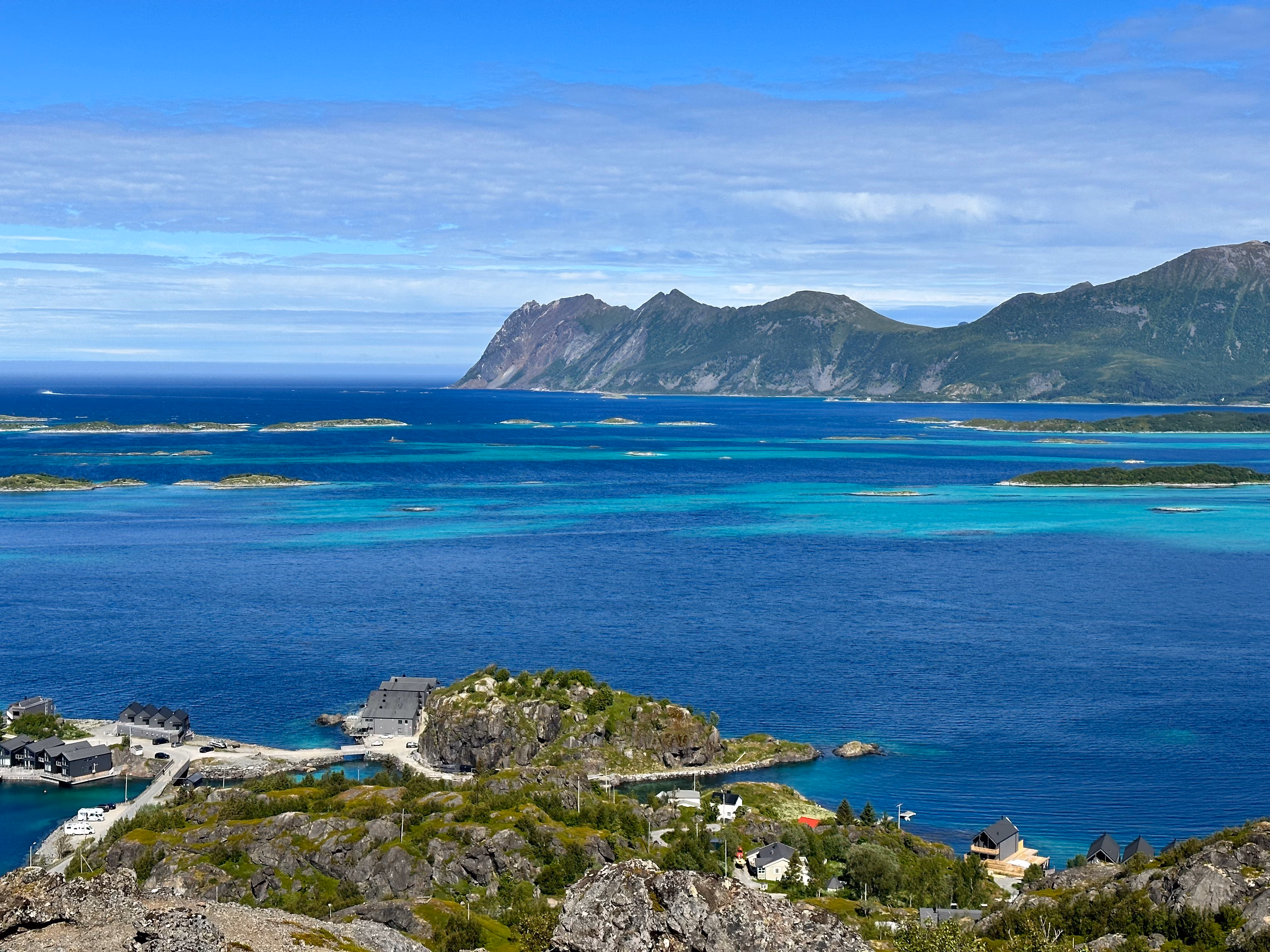 High-angle panoramic view of turquoise fjord waters, green islands, and sandy beaches.