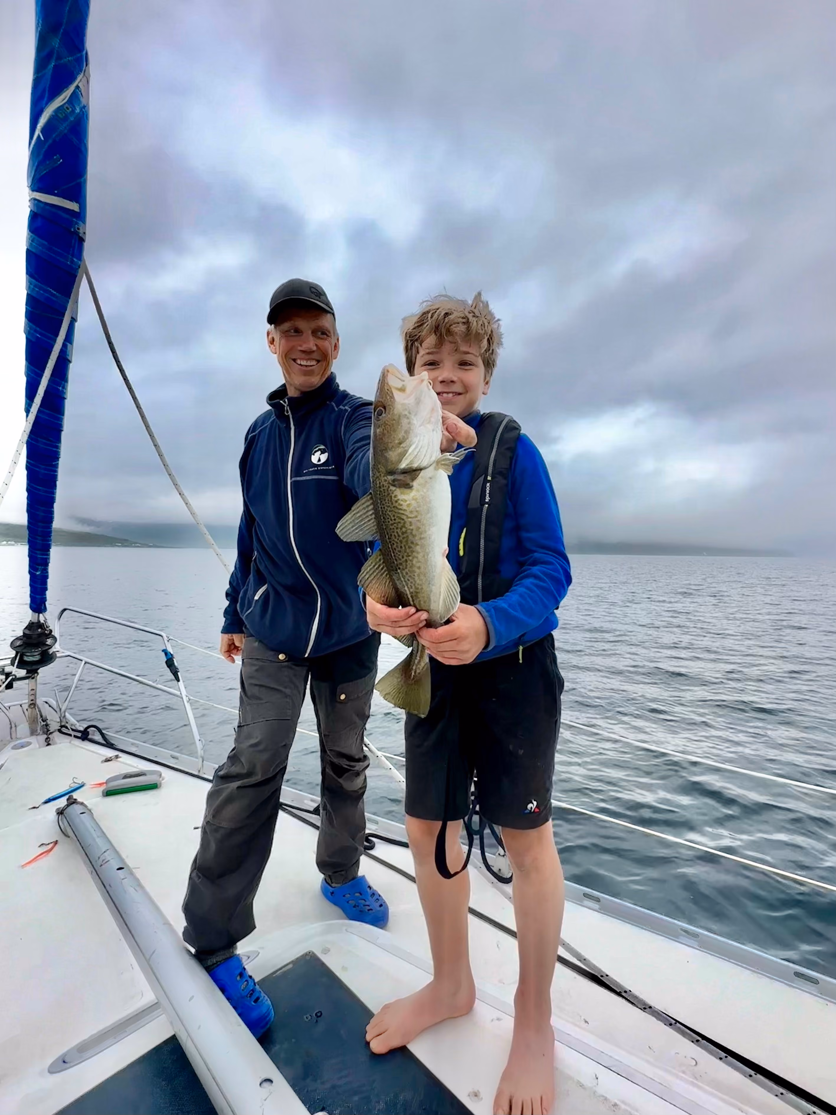 Person standing on a sailboat deck proudly holding a freshly caught fish.
