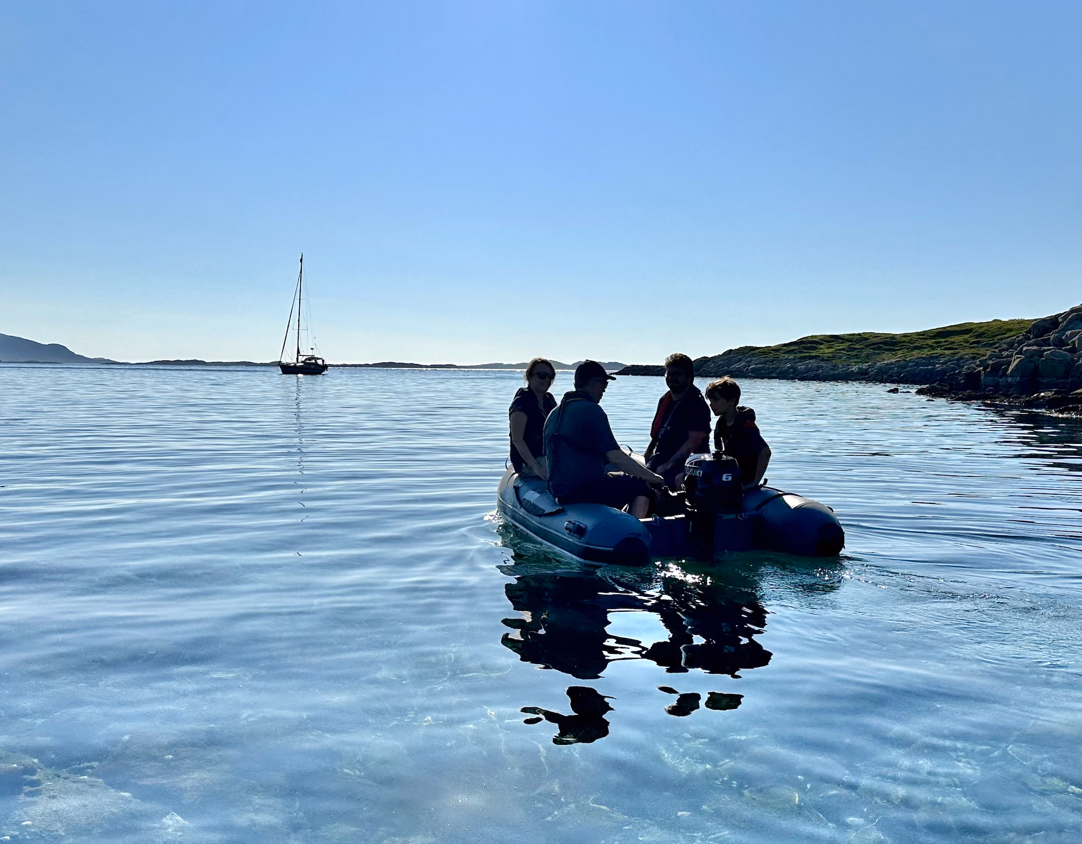 Small inflatable dinghy with passengers floating on calm ocean waters near distant mountains.