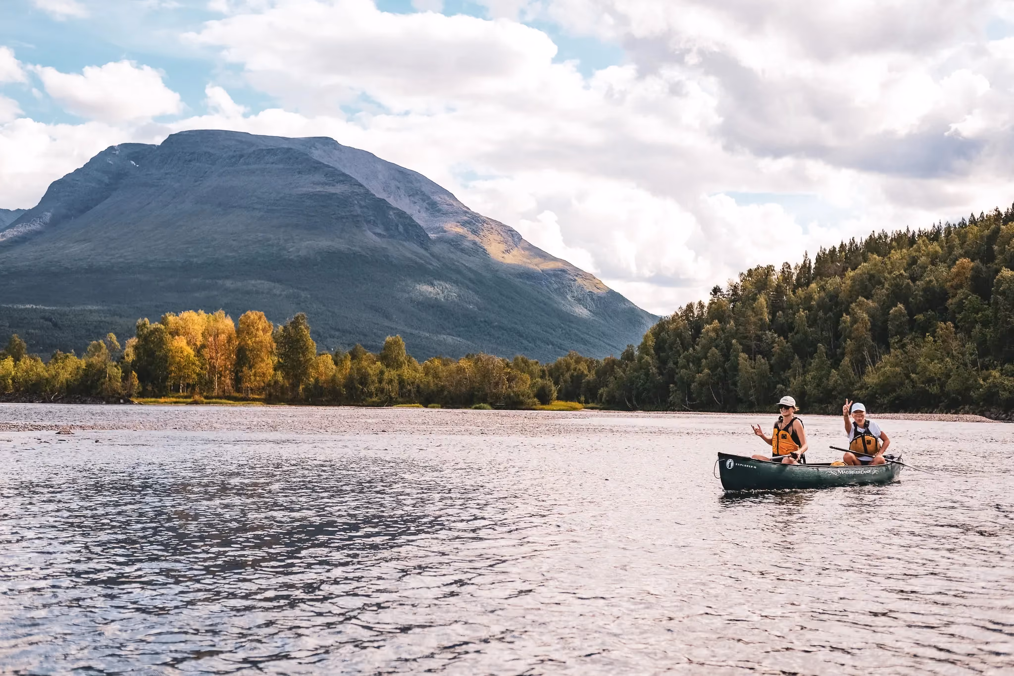 Canoeists paddling across a calm lake toward scenic mountain slopes.