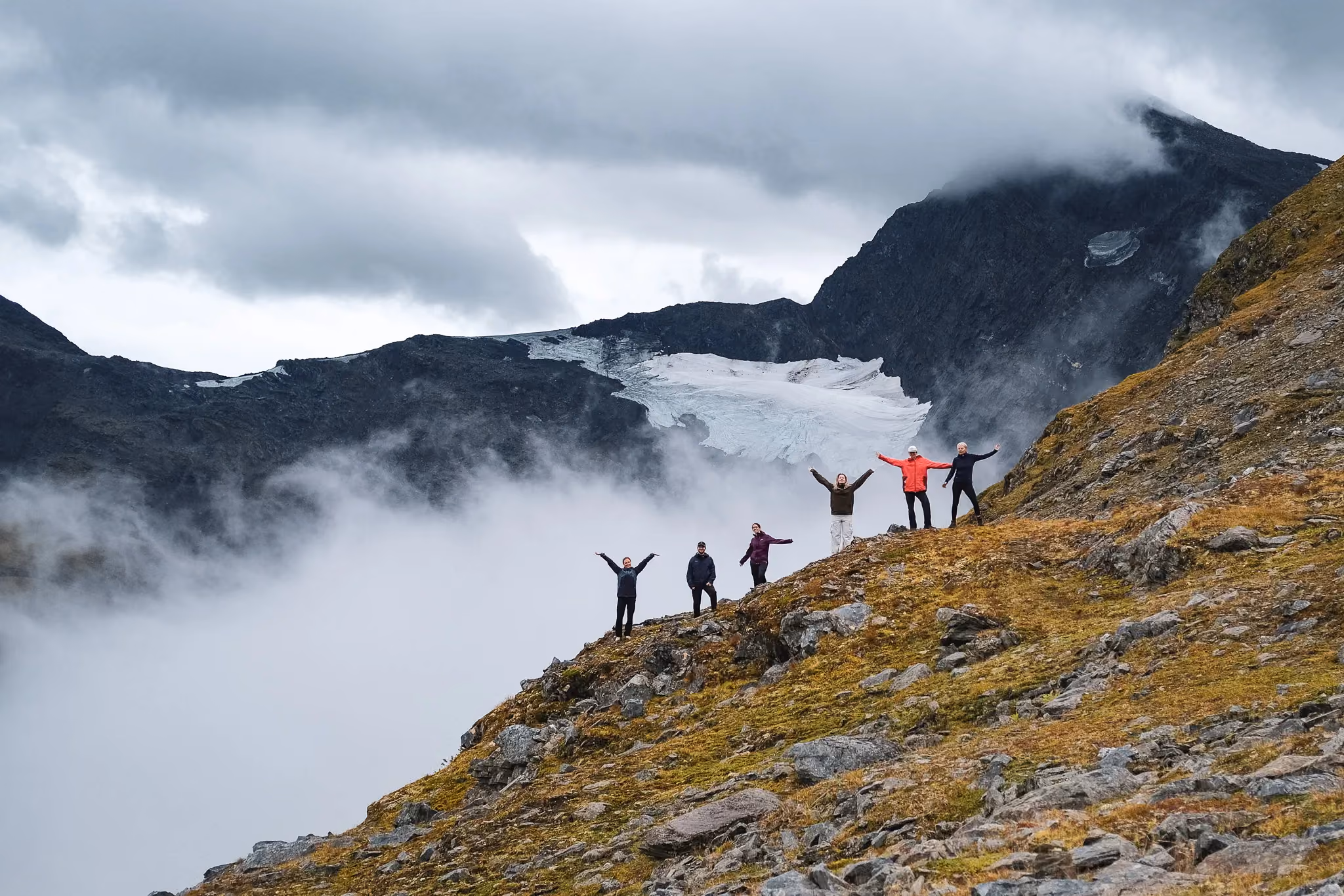 Hikers walking along a mountain path framed by dramatic low clouds and mist.