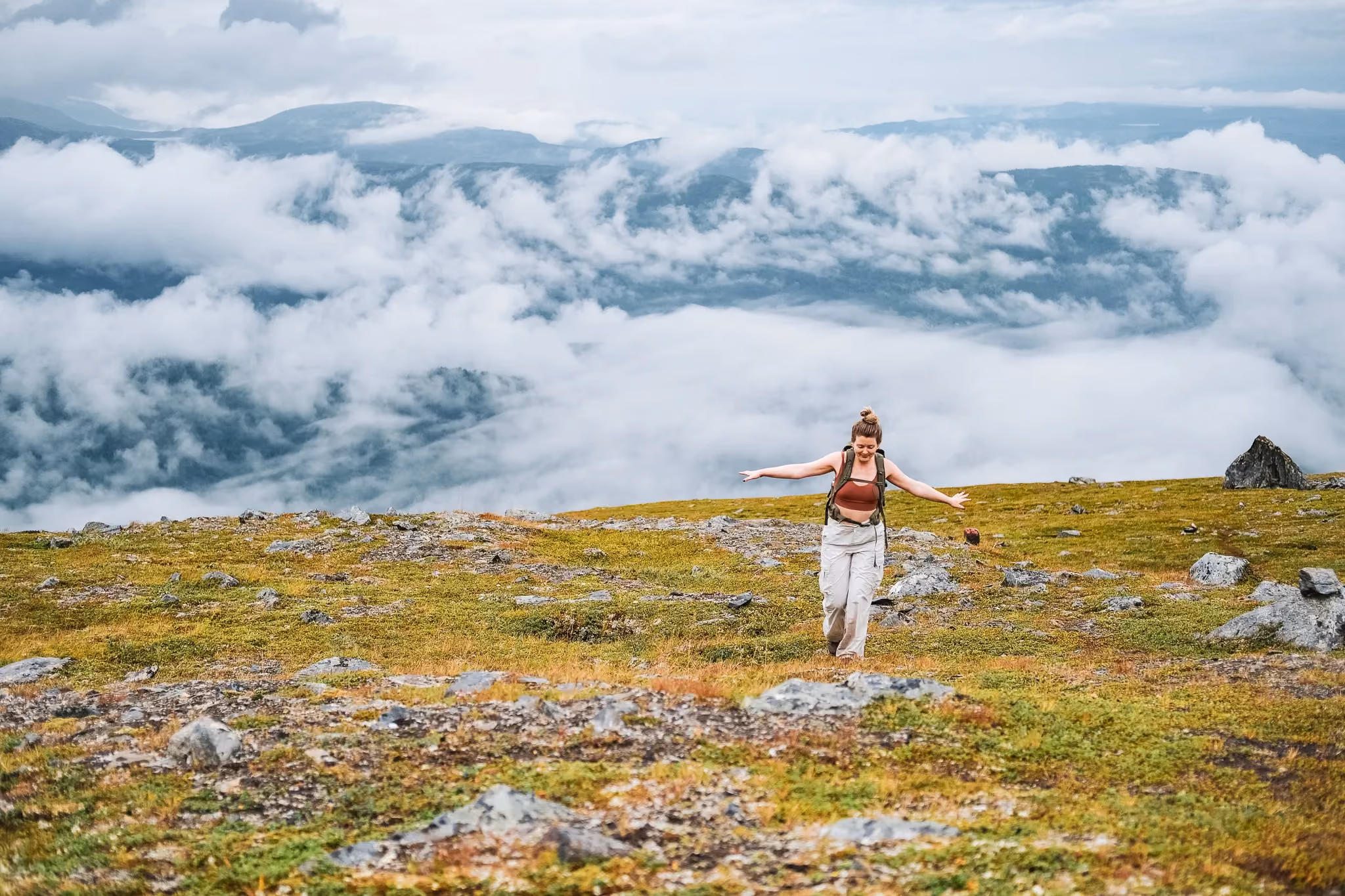 Hiker standing on a mountain plateau high above a sea of white clouds.