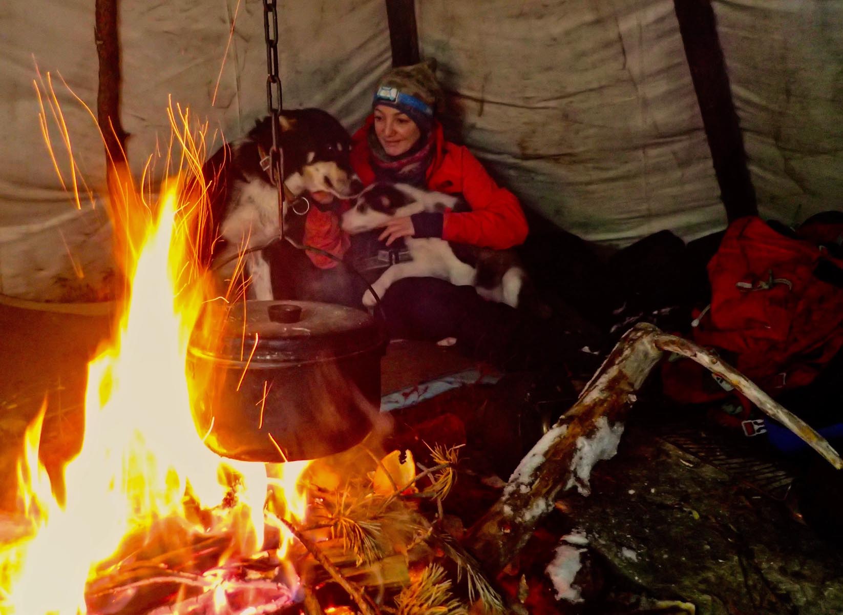 Group of people sitting around a warm campfire inside a wooden shelter.