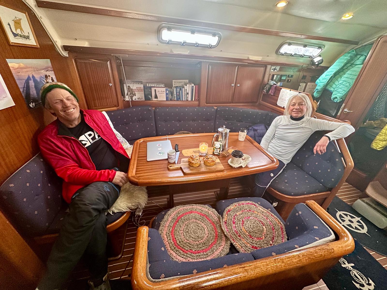 Group of people sitting around a dining table inside a cozy wooden sailboat cabin.