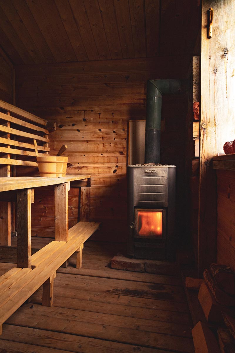 Wooden sauna interior featuring tiered benches and a glowing wood-burning stove.