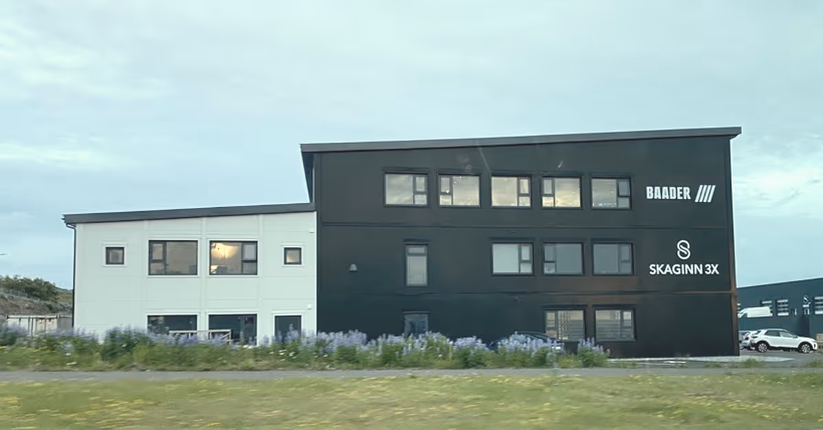 Modern two-tone office building with white and dark grey sections, featuring windows and logos for BAADER and SKAGINN 3X on the dark facade.