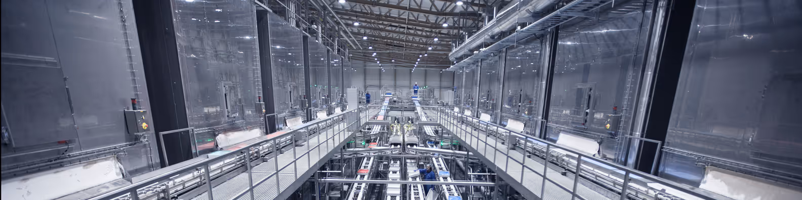 Interior of a large industrial facility with metal walkways and conveyor belts running through the center.