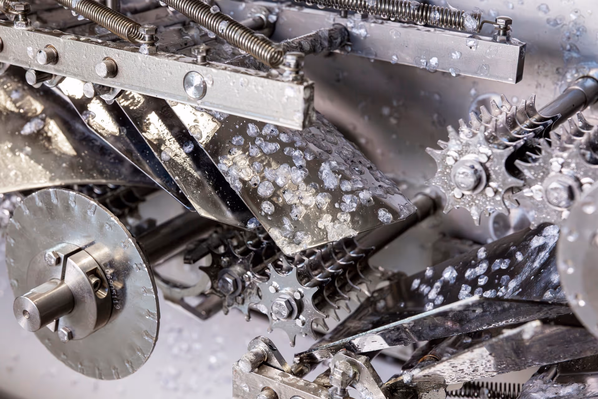 Close-up of a stainless steel machine with gears and components covered in ice or frozen particles.