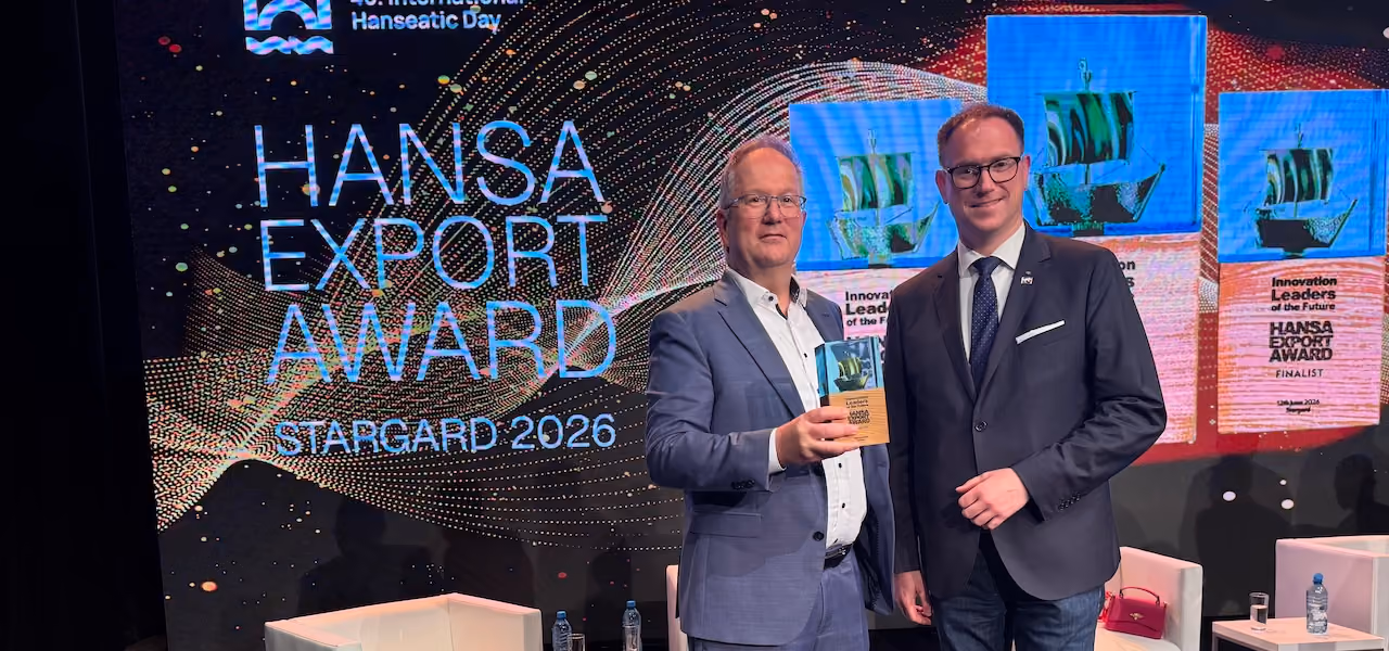 Two men in suits standing, one holding a HANSA Export Award trophy in front of event signage.
