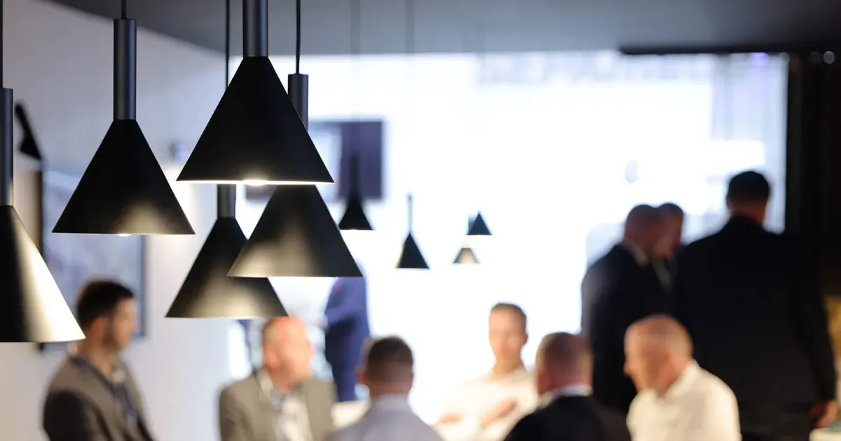 Cluster of modern black pendant lamps with conical shades hanging from the ceiling in a softly lit indoor space with blurred people in the background.