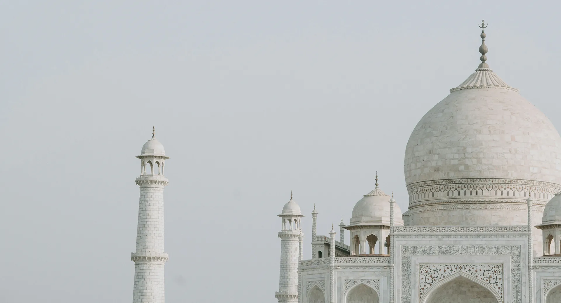 Partial view of the white marble Taj Mahal with its large main dome and two adjacent minarets under a clear sky.