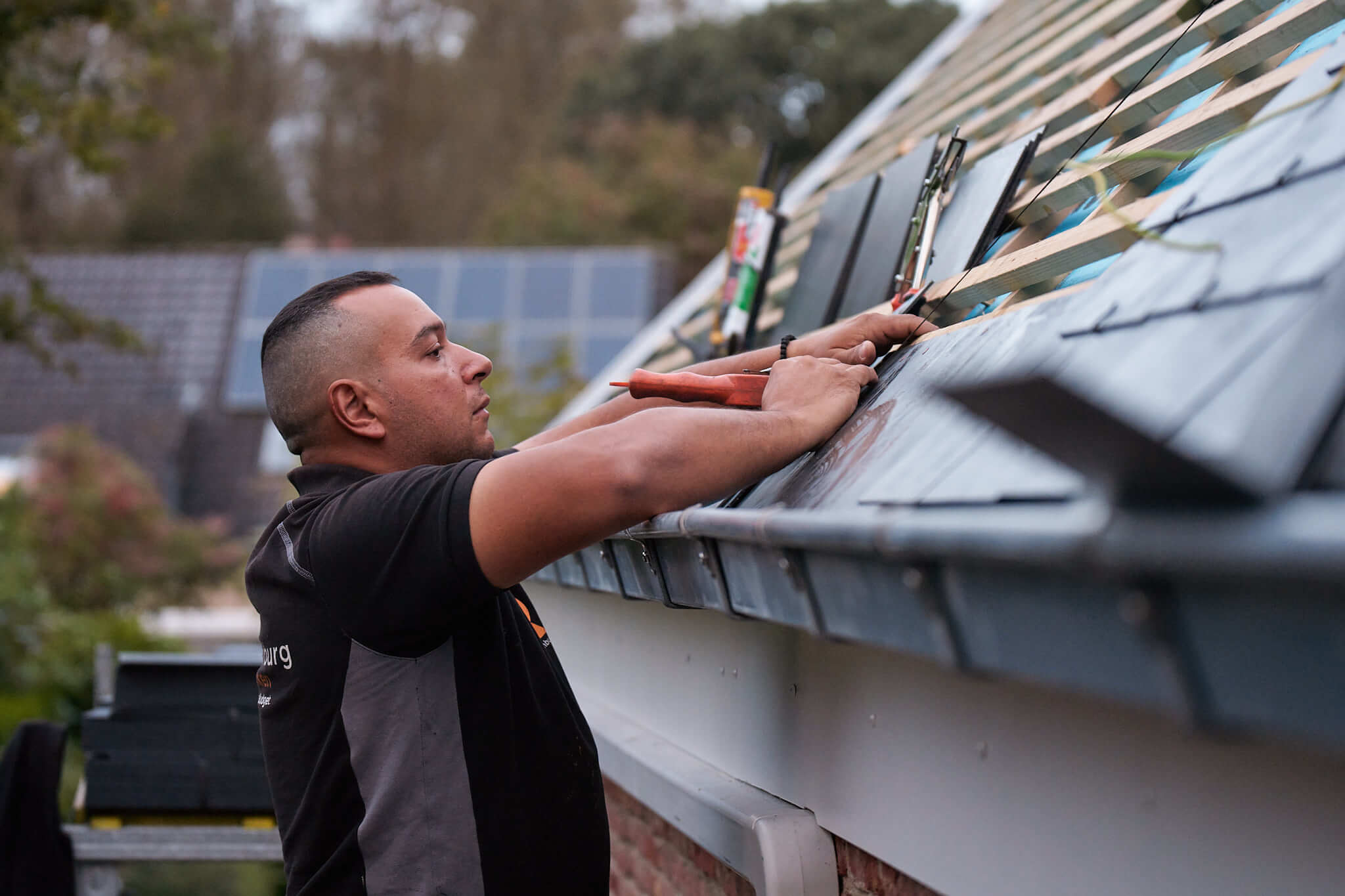 Dakwerker van Roozenburg Dakwerken aan de slag aan een dakgoot van een dak met leien