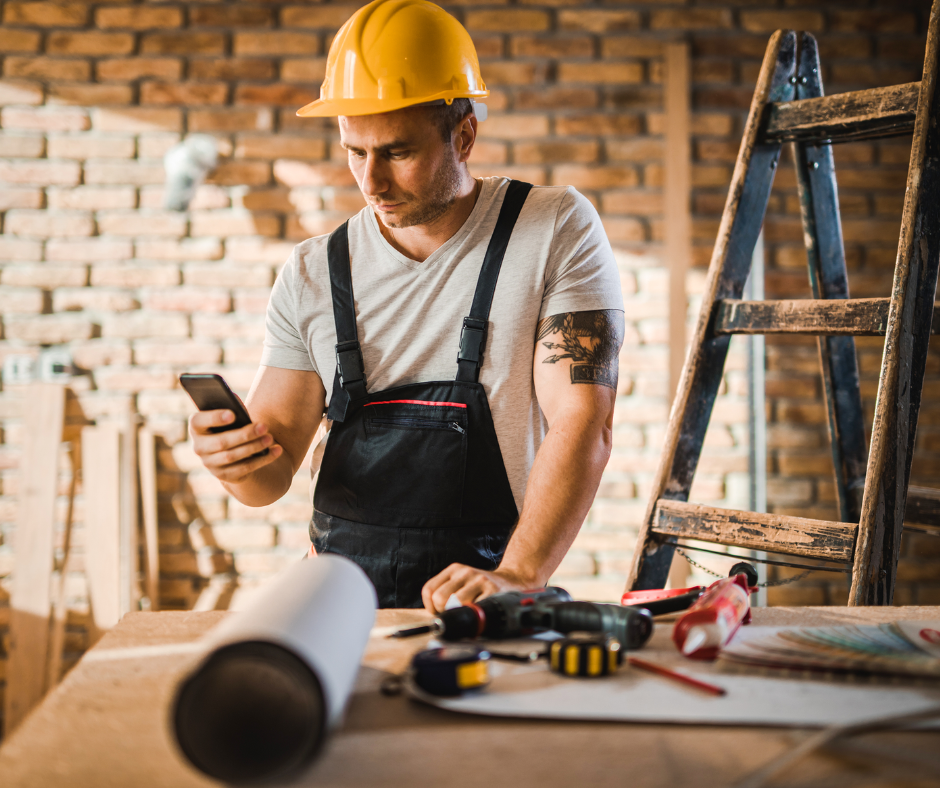 Ein Handwerker, der mit seinem Smartphone in der Baustelle steht.