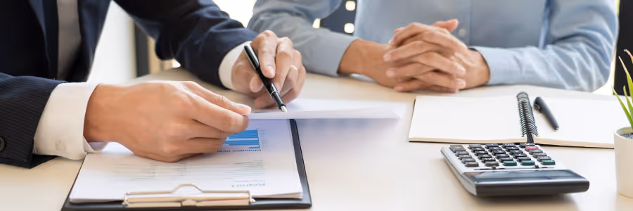 Two people reviewing a financial document with a calculator and notebook on the desk.