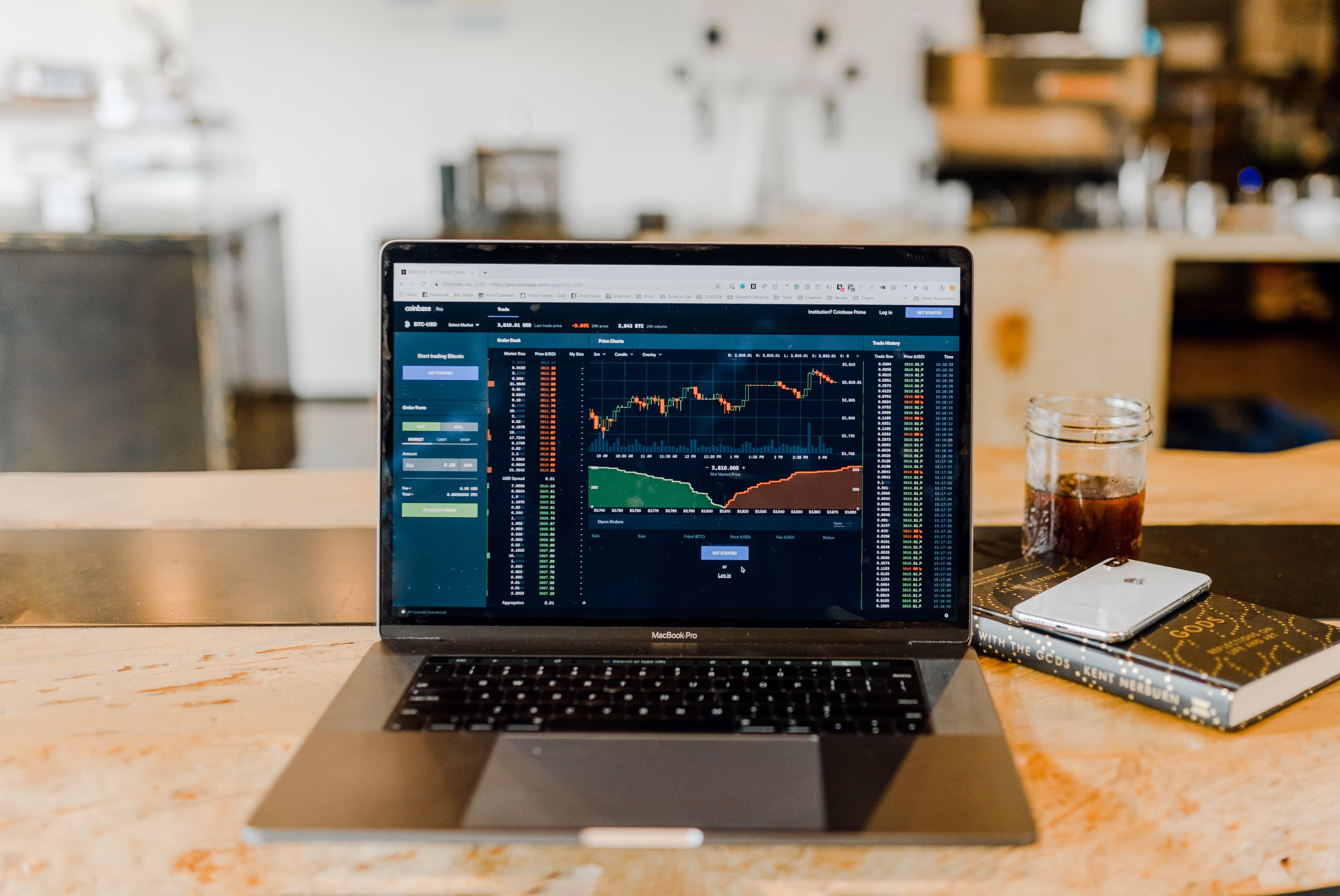 Open MacBook Pro laptop on wooden table displaying cryptocurrency trading chart and order book.