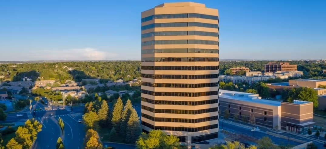 Tall office building with horizontal stripes surrounded by trees and roads under a clear blue sky.