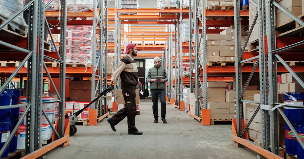 Two warehouse workers checking inventory counts in a distribution aisle