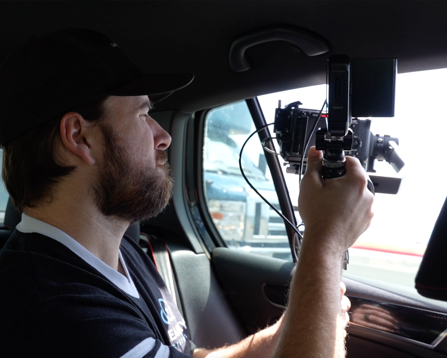 behind the scenes photo of man filming a vehicle while in a moving car
