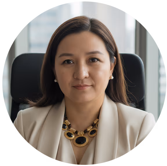 Professional Asian woman with long hair wearing a beige blazer and statement necklace, seated in office.
