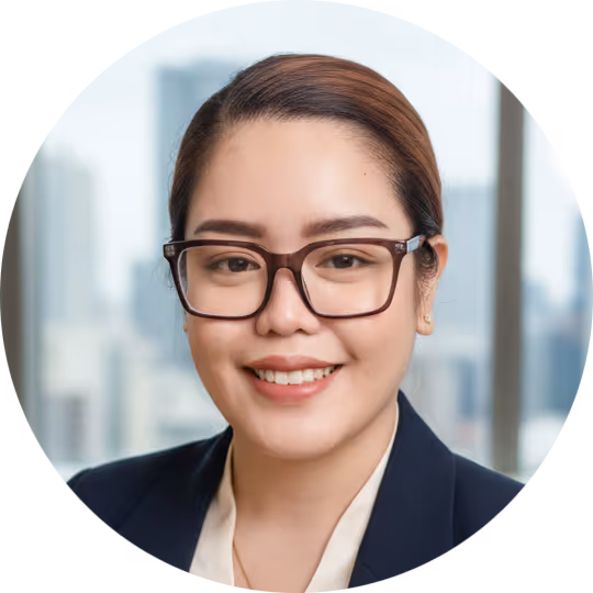 Smiling woman with glasses in a navy blazer with a blurred cityscape background.