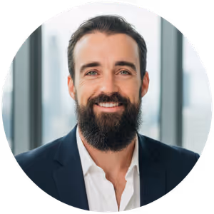 Smiling man with beard and dark hair wearing white shirt and dark blazer in front of a blurred window.