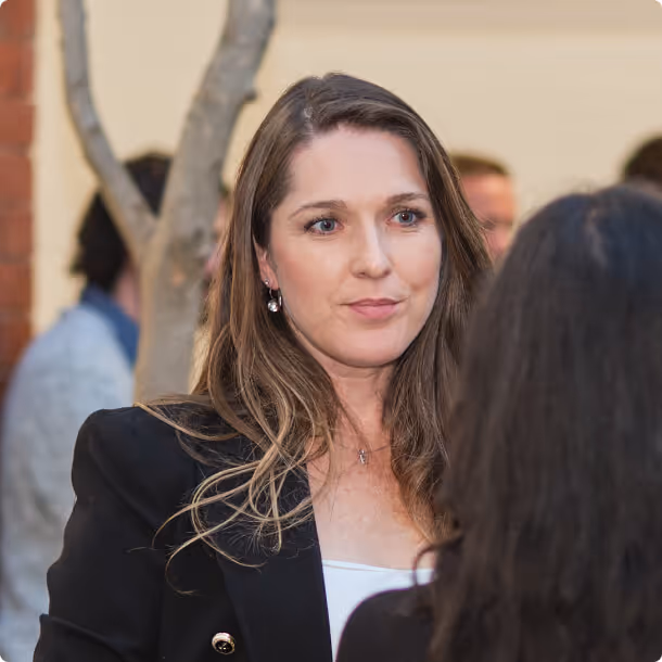 A woman in a black blazer talking to another woman.