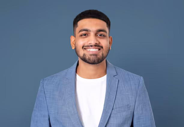 Nuori mies hymyilee sinisen taustan edessä, pukeutuneena vaaleansiniseen bleiseriin ja valkoiseen T-paitaan.