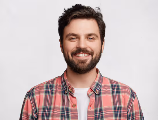 Hymyilevä mies, jolla on tumma parta ja tummat hiukset, pukeutuneena punavihreään ruudulliseen paitaan ja valkoiseen t-paitaan.