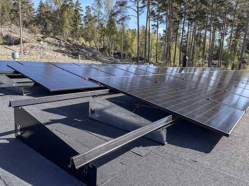 Aurinkopaneelijärjestelmä asennettuna kaltevalle mustalle katolle metsämaisemassa.