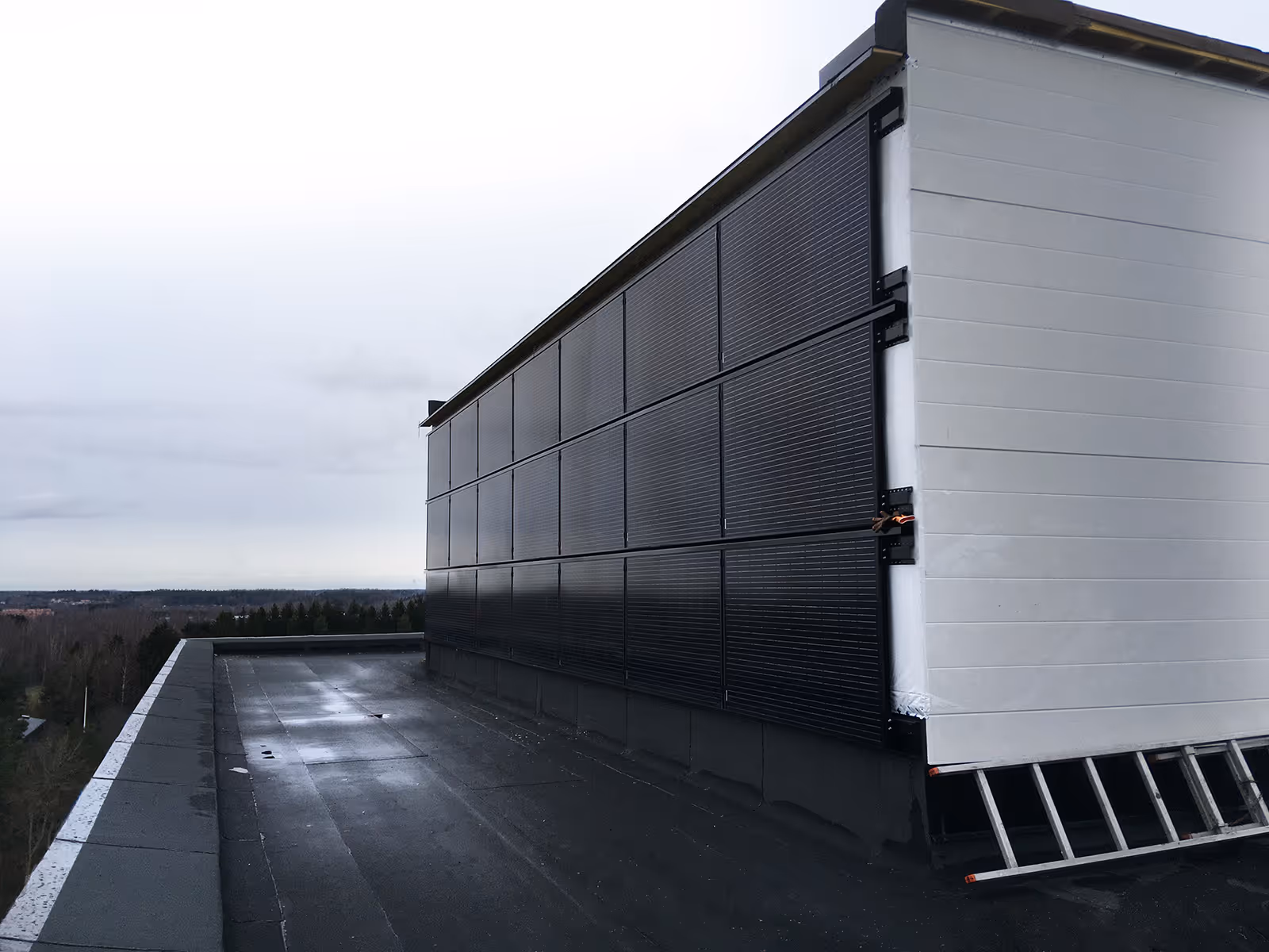 Katon sivu, jossa on asennettu mustia aurinkopaneeleja rakennuksen seinälle pilvisenä päivänä.