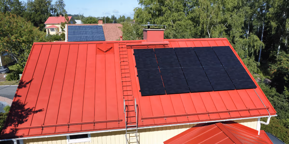 Mustat aurinkopaneelit punaisella harjakatolla Aurinkotekniikan toimittamana