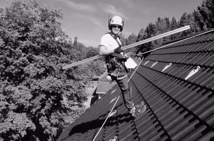 Katolla turvavaljaissa seisova Aurinkopaneeliasentaja kantaa pitkää asennuskiskoa