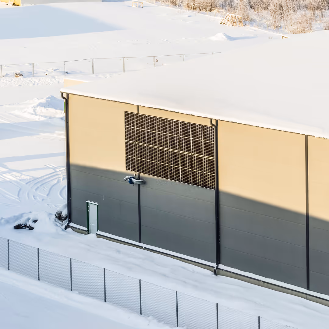 Teollisuusrakennus lumisessa ympäristössä auringonvalossa, näkyvissä aurinkopaneelit seinällä