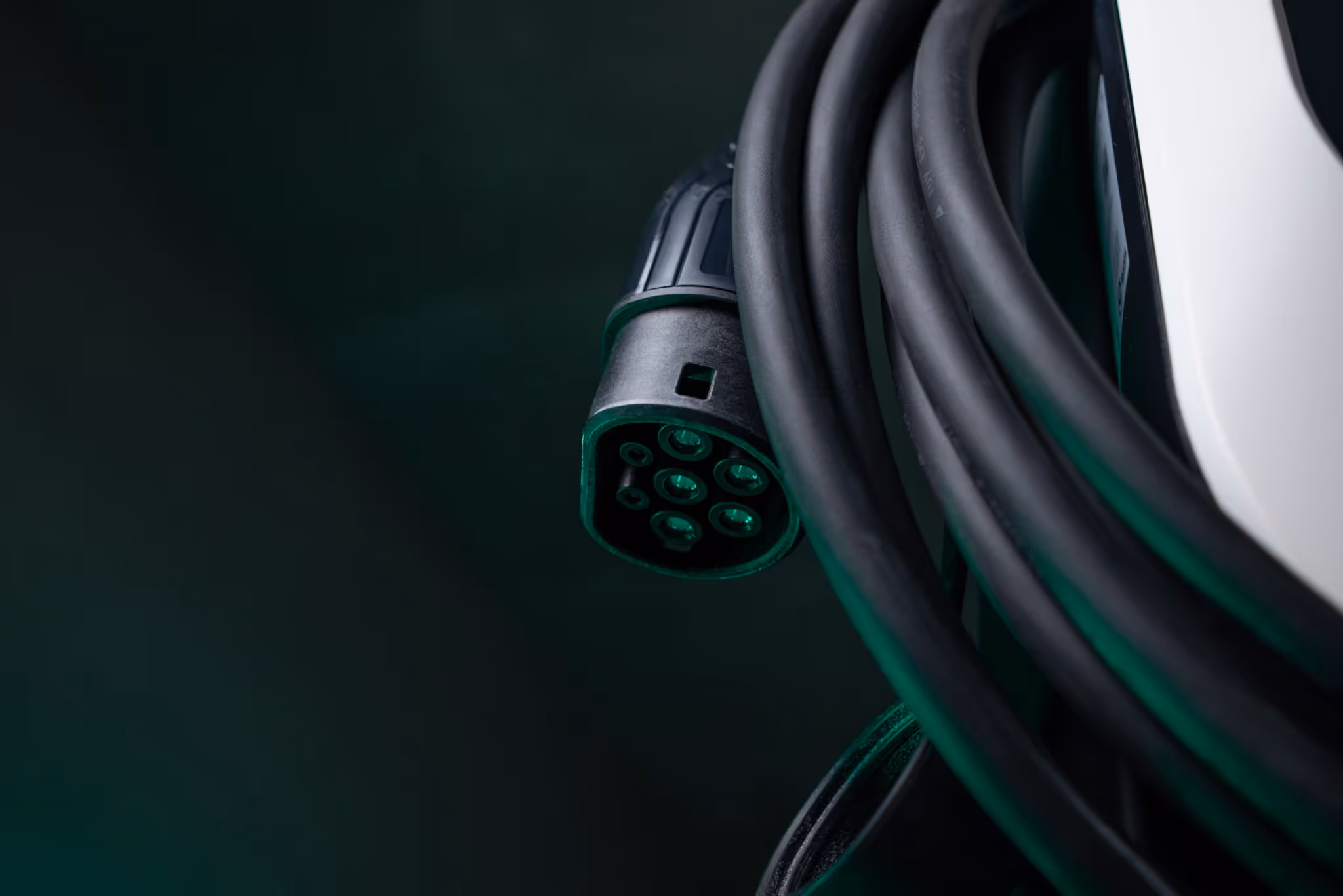 Lähikuva sähköauton latauskaapelin liittimestä ja mustasta johdosta tummalla taustalla. Volt time One